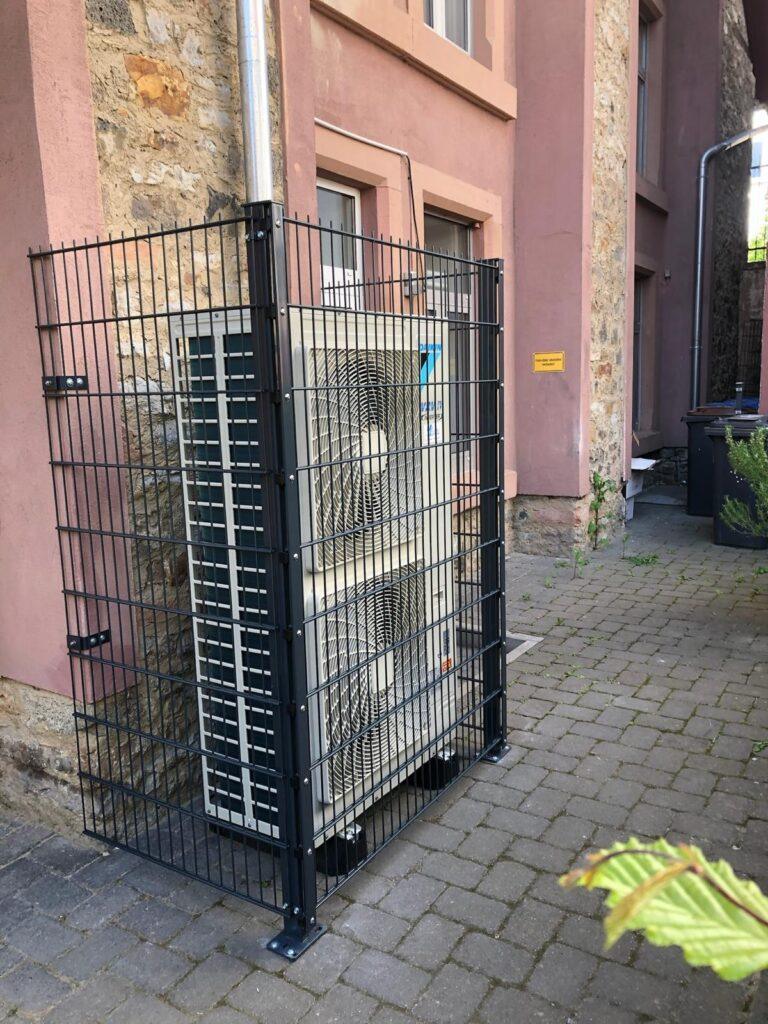 Klimaanlage, die in einem stabilen Schutzgitter im Freien installiert ist, um sie vor äußeren Einflüssen zu schützen.