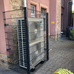 Klimaanlage, die in einem stabilen Schutzgitter im Freien installiert ist, um sie vor äußeren Einflüssen zu schützen.